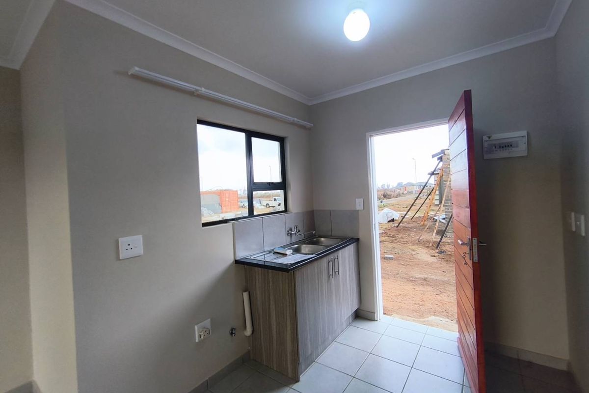 A compact kitchen area featuring a single sink unit with cabinetry, tiled flooring, and direct access to the exterior.