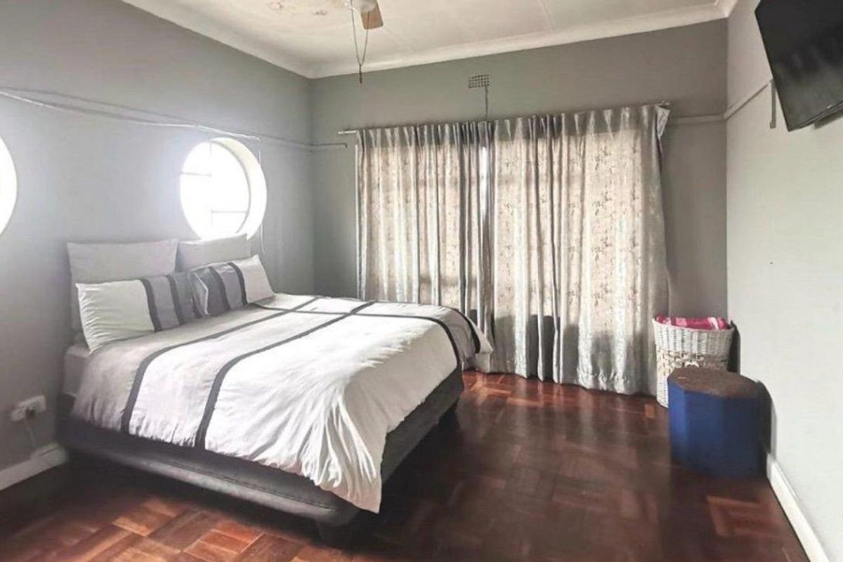 A spacious bedroom featuring classic parquet flooring, unique circular windows, and large curtains, offering a comfortable and well-lit living space.