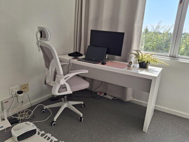A functional home office space featuring neutral carpet flooring, large window with curtain tracks, and accessible electrical outlets.