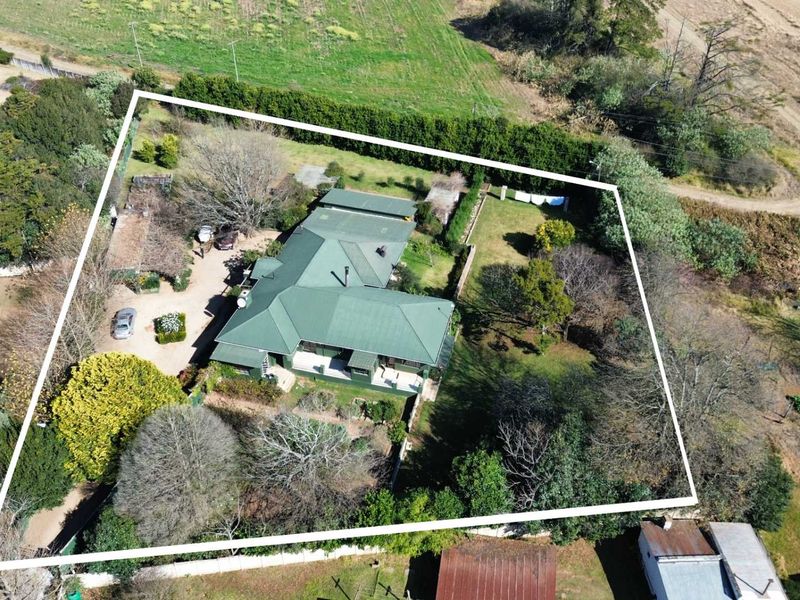 Aerial view of a residential property featuring a metal roof, expansive garden, and driveway, set within a rural or semi-rural landscape.