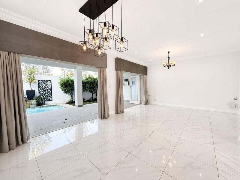 Spacious, light-filled living area featuring polished marble-look floor tiles, elegant lighting fixtures, and seamless access to the outdoor patio and pool area.