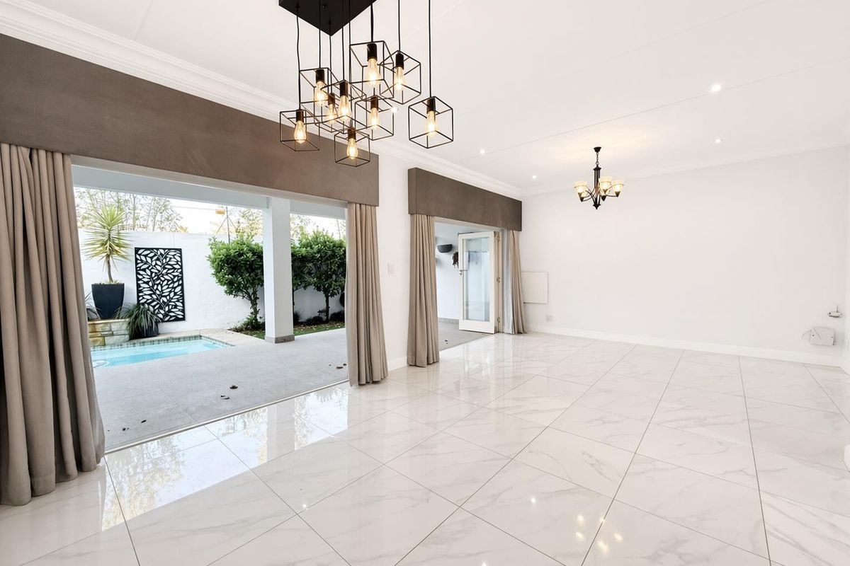 Spacious, light-filled living area featuring polished marble-look floor tiles, elegant lighting fixtures, and seamless access to the outdoor patio and pool area.