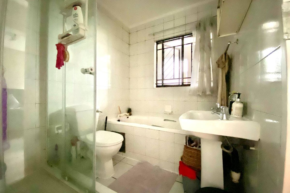 A functional bathroom featuring a pedestal basin, a bathtub with tiled surround, and a separate glass-enclosed shower area with white wall tiling.