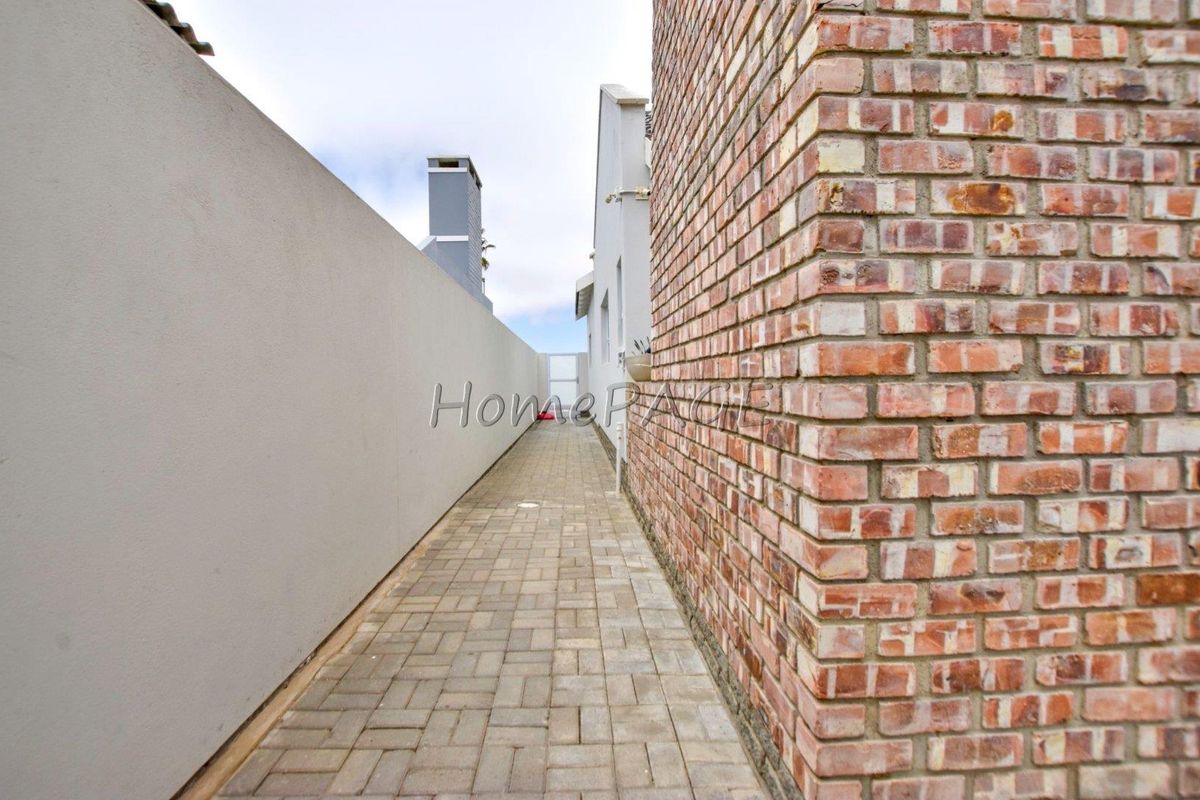 A narrow side passage featuring paved flooring, a rendered boundary wall, and an exposed brick exterior wall of the main dwelling.