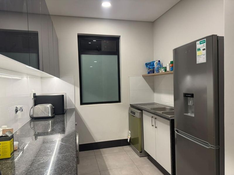 A functional scullery featuring granite countertops, built-in cabinetry, a stainless steel sink, and tiled flooring, providing additional workspace and storage.