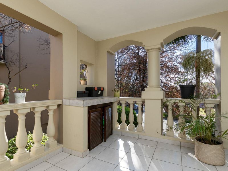 A covered balcony featuring classic arched columns, a decorative balustrade, tiled flooring, and built-in storage cabinetry.