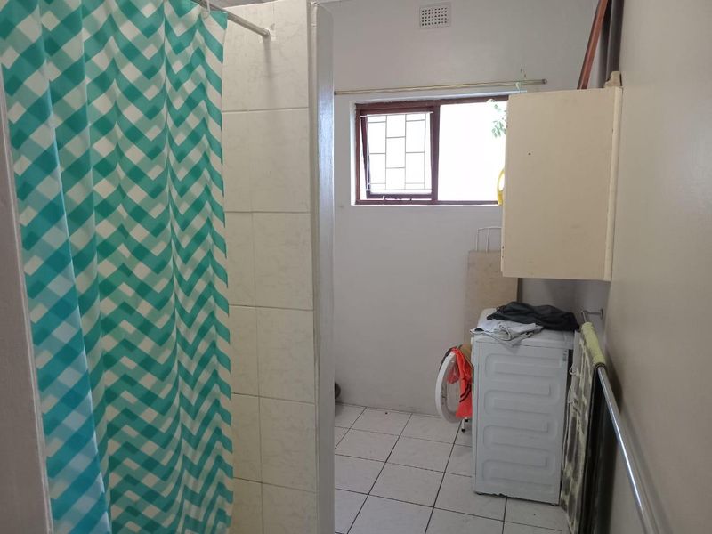 A functional laundry area featuring tiled flooring, a wall-mounted storage cabinet, and a window with security bars.