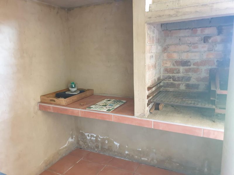 Outdoor patio area featuring a built-in brick braai with tiled prep counter and flooring, requiring some cosmetic maintenance to the wall finishes.