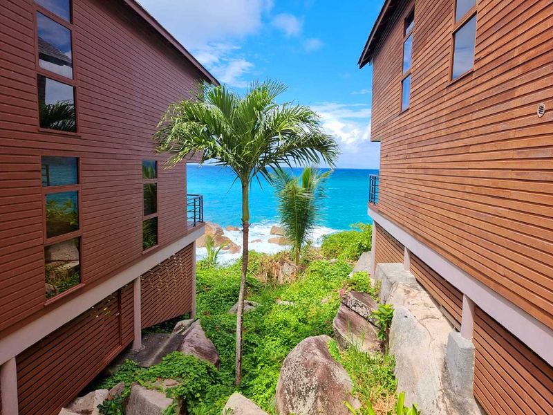 A scenic view between two timber-clad commercial structures, showcasing lush tropical landscaping and a direct outlook over the ocean.