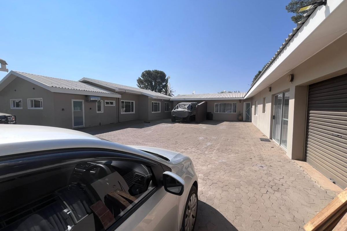 A spacious paved courtyard area providing access to multiple building sections, including a garage with a roller shutter door and sliding glass entry points.