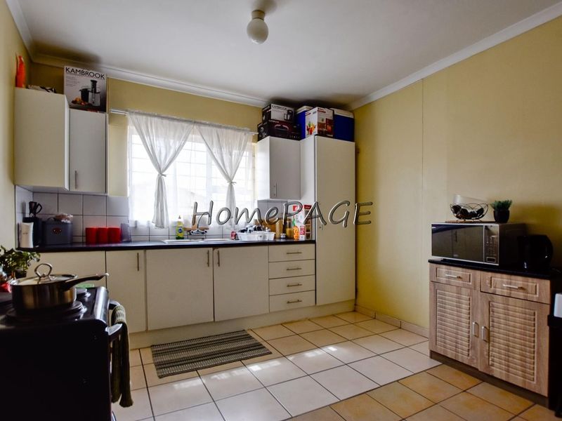 A functional kitchen featuring built-in cabinetry, laminate countertops, a stainless steel sink, and tiled flooring with security bars on the window.