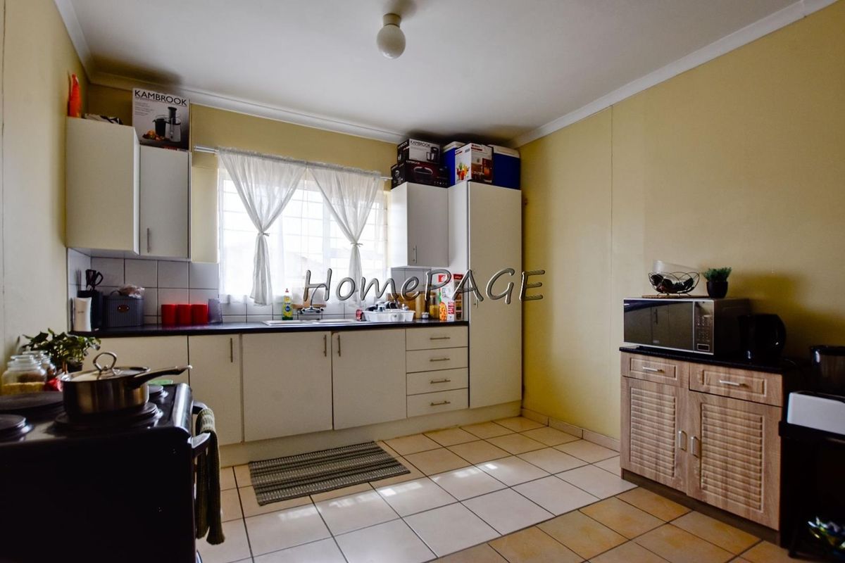 A functional kitchen featuring built-in cabinetry, laminate countertops, a stainless steel sink, and tiled flooring with security bars on the window.