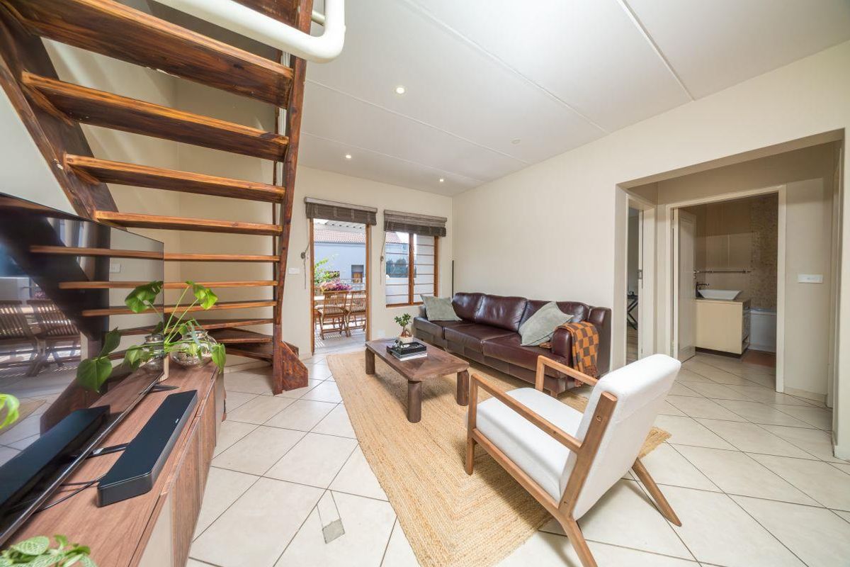 Open-plan living area featuring a wooden staircase, tiled flooring, and direct access to an outdoor patio space.