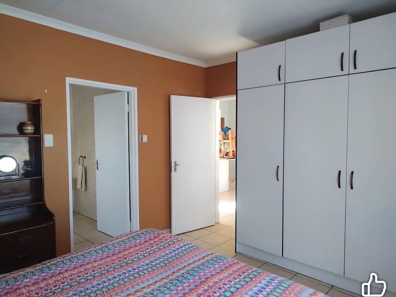 A bedroom featuring built-in white wardrobes, tiled flooring, and access to adjacent rooms through internal doorways.