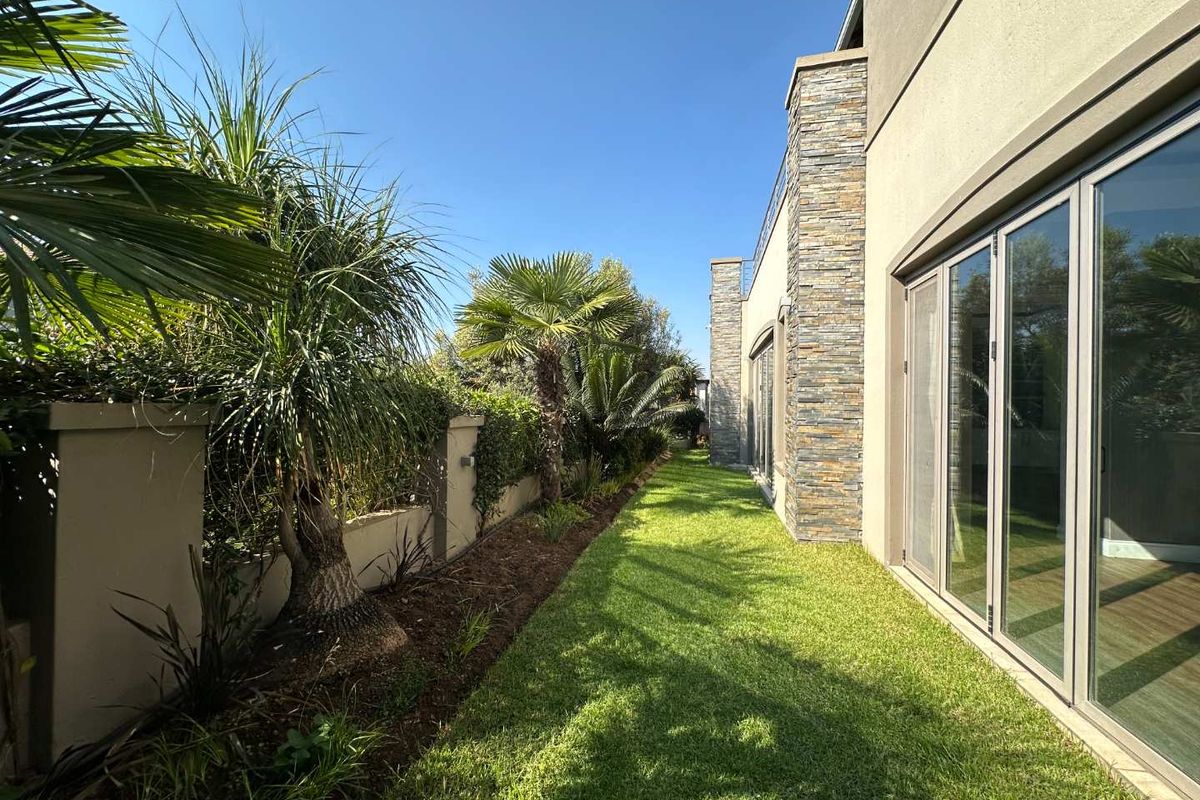 A well-maintained rear garden featuring a manicured lawn, landscaped border, and modern exterior facade with stone cladding and large glass sliding doors.