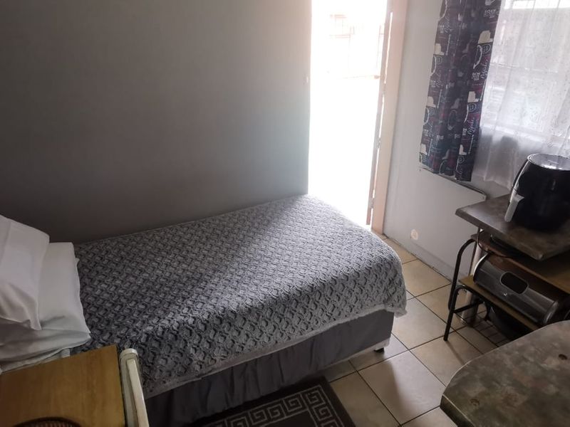 A compact bedroom featuring tiled flooring and natural light access through a window and door.