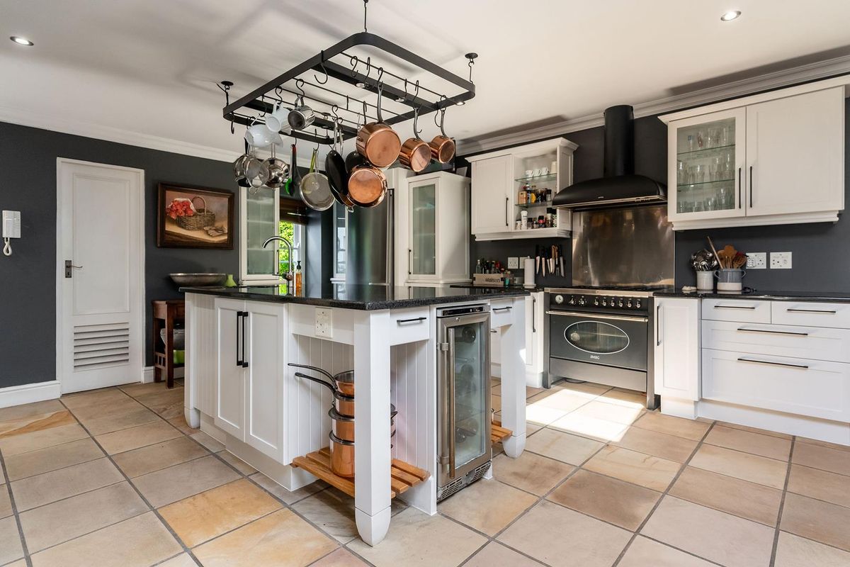 A well-appointed kitchen featuring a central island with a wine cooler, granite countertops, white cabinetry, and a professional-style range cooker with an extractor hood.