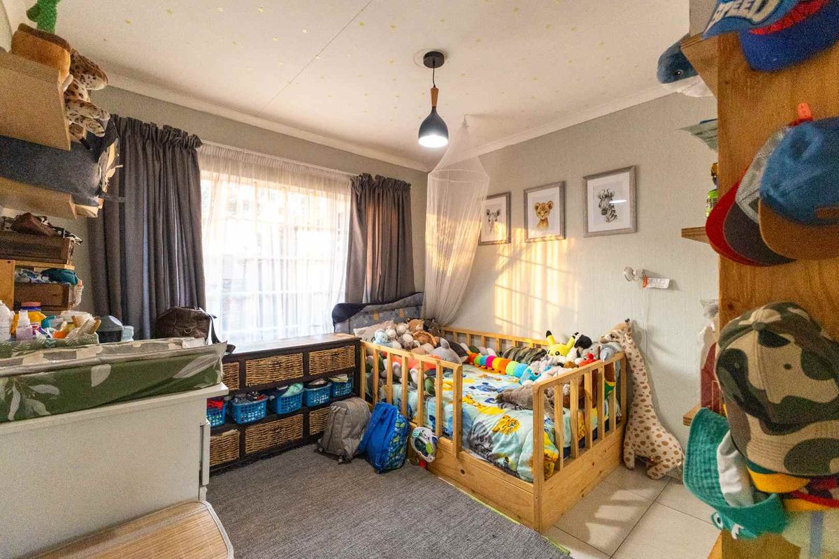 A functional bedroom featuring tiled flooring, a central pendant light, and large windows with curtain rails, providing a comfortable living space.