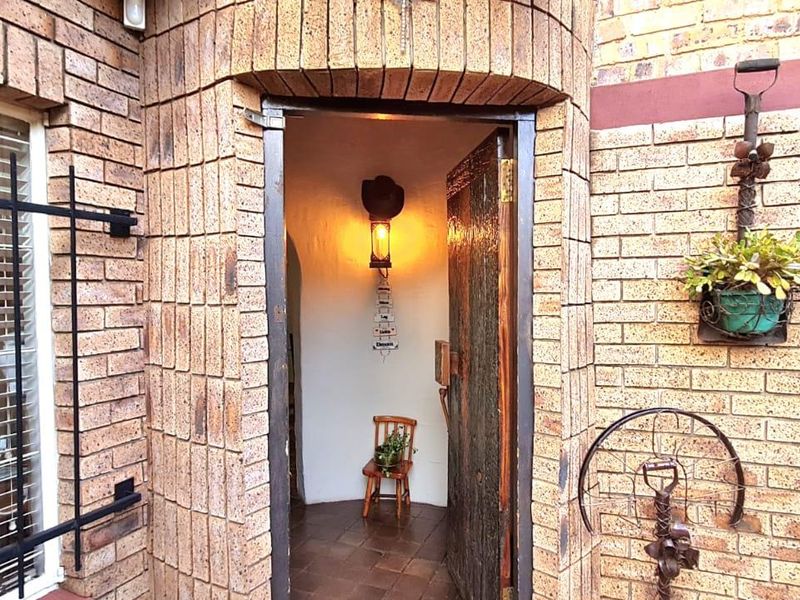 A rustic entrance featuring a face brick facade, a solid timber door, and security bars over the window.