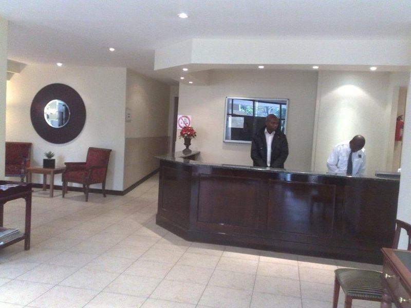 A building entrance lobby featuring a dark wood reception desk, tiled flooring, and recessed ceiling lighting.
