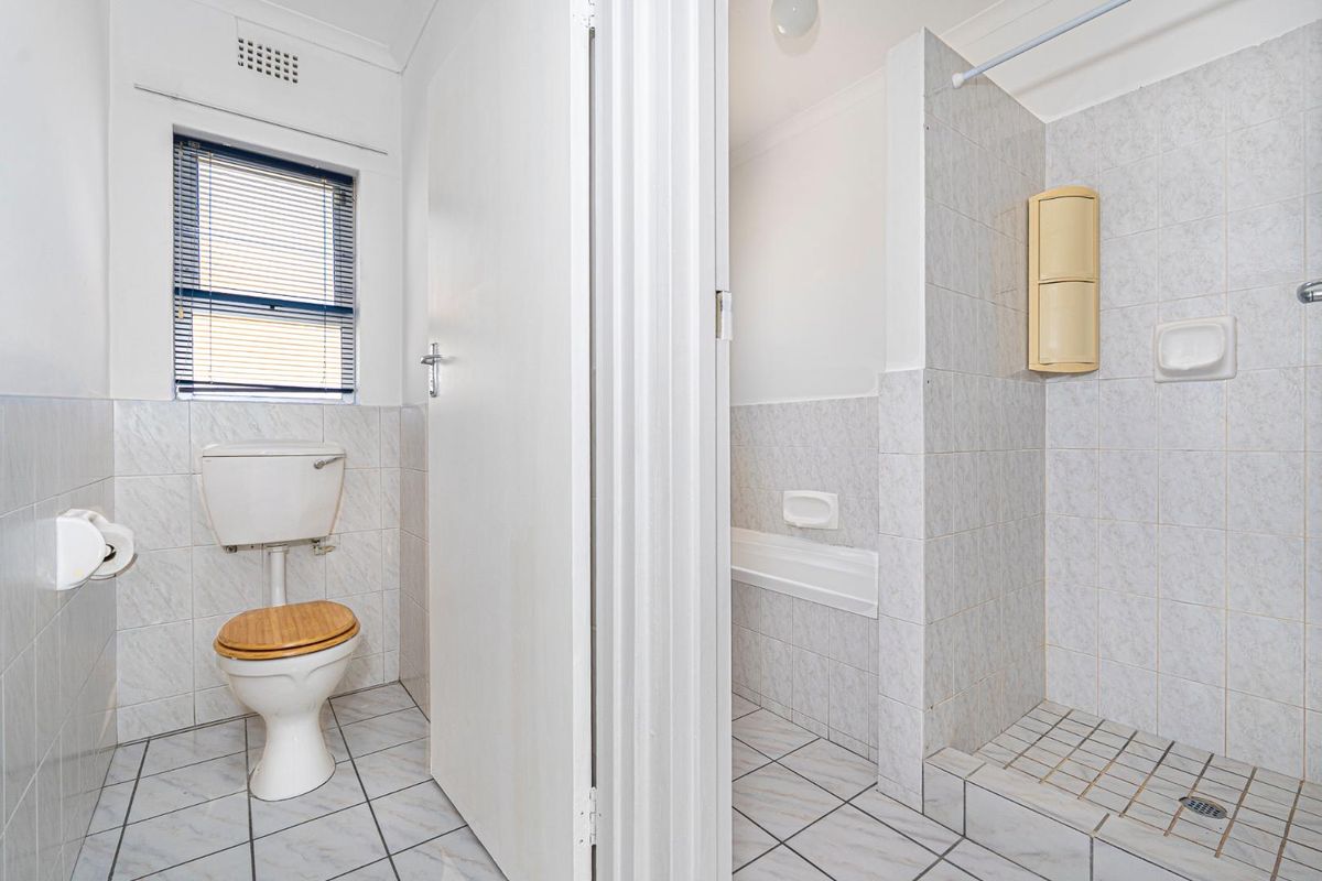 A functional bathroom featuring a separate toilet area, a tiled shower enclosure, and neutral wall tiling throughout.