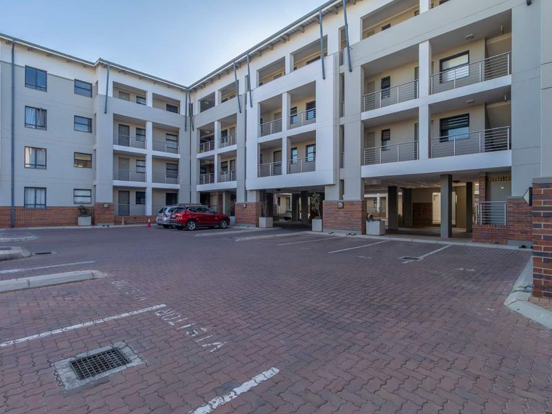 Modern apartment complex exterior featuring a paved parking area, brick and render facade, and multiple levels of private balconies.