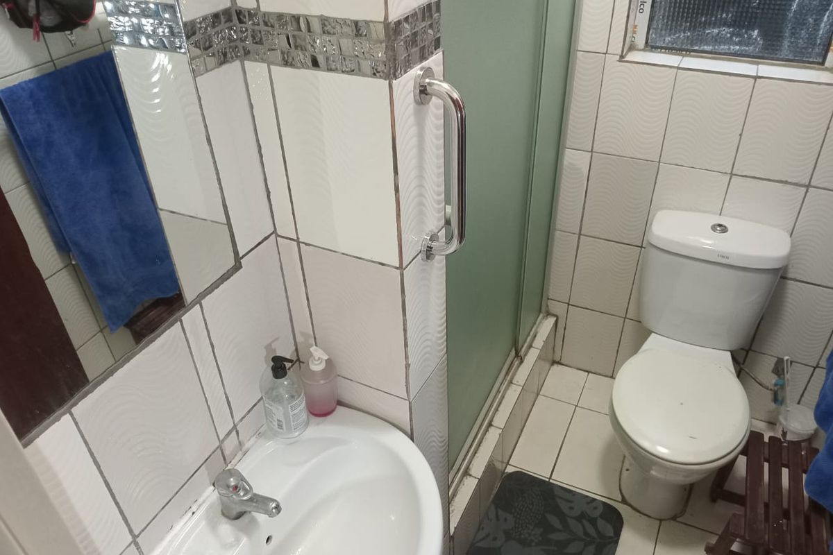 Compact bathroom featuring a white pedestal basin, a toilet, and a glass-enclosed shower stall with wall-mounted grab rails.