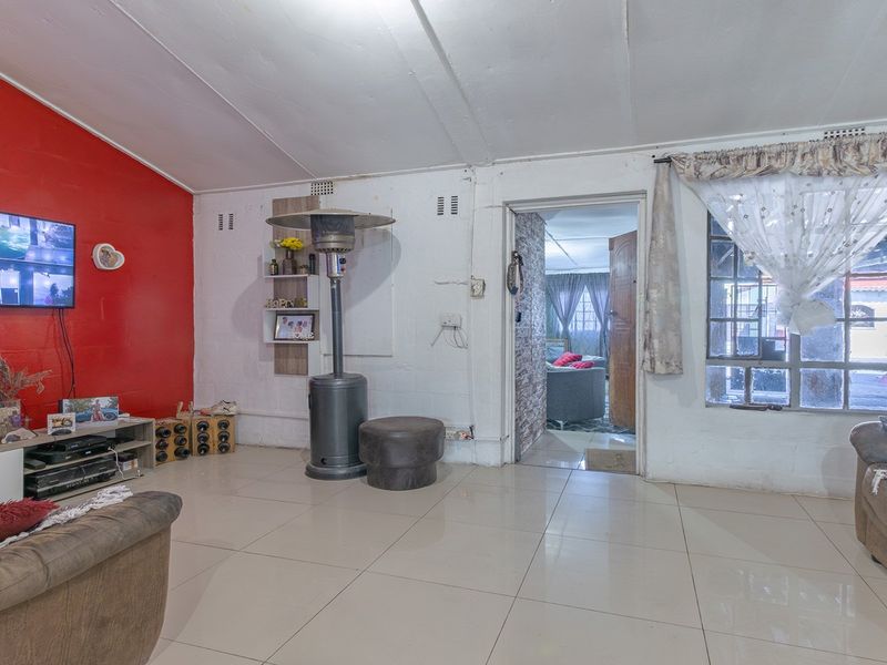 A living room featuring tiled flooring and a bold red accent wall, offering a functional space with potential for cosmetic updates.
