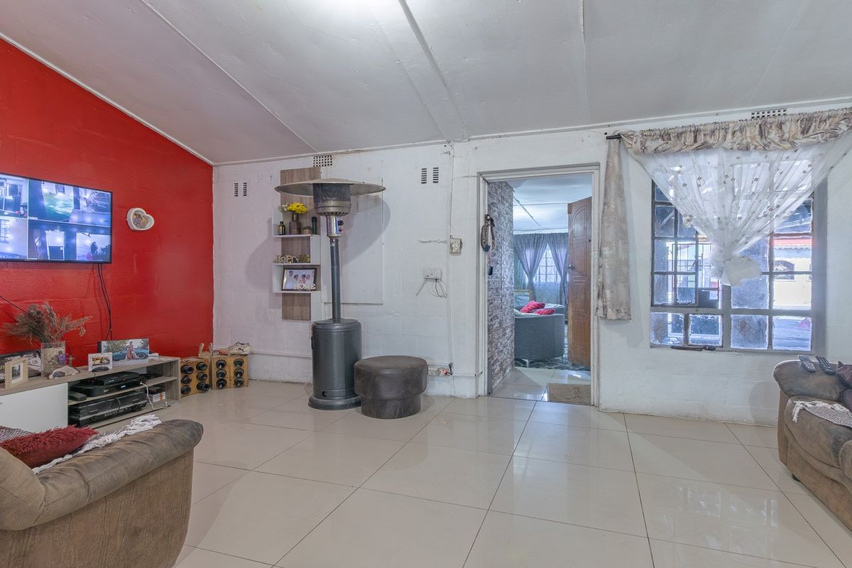 A living room featuring tiled flooring and a bold red accent wall, offering a functional space with potential for cosmetic updates.