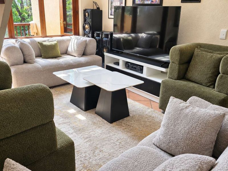 A comfortable living room featuring terracotta floor tiles, wooden window frames, and access to an adjacent outdoor area via a staircase.