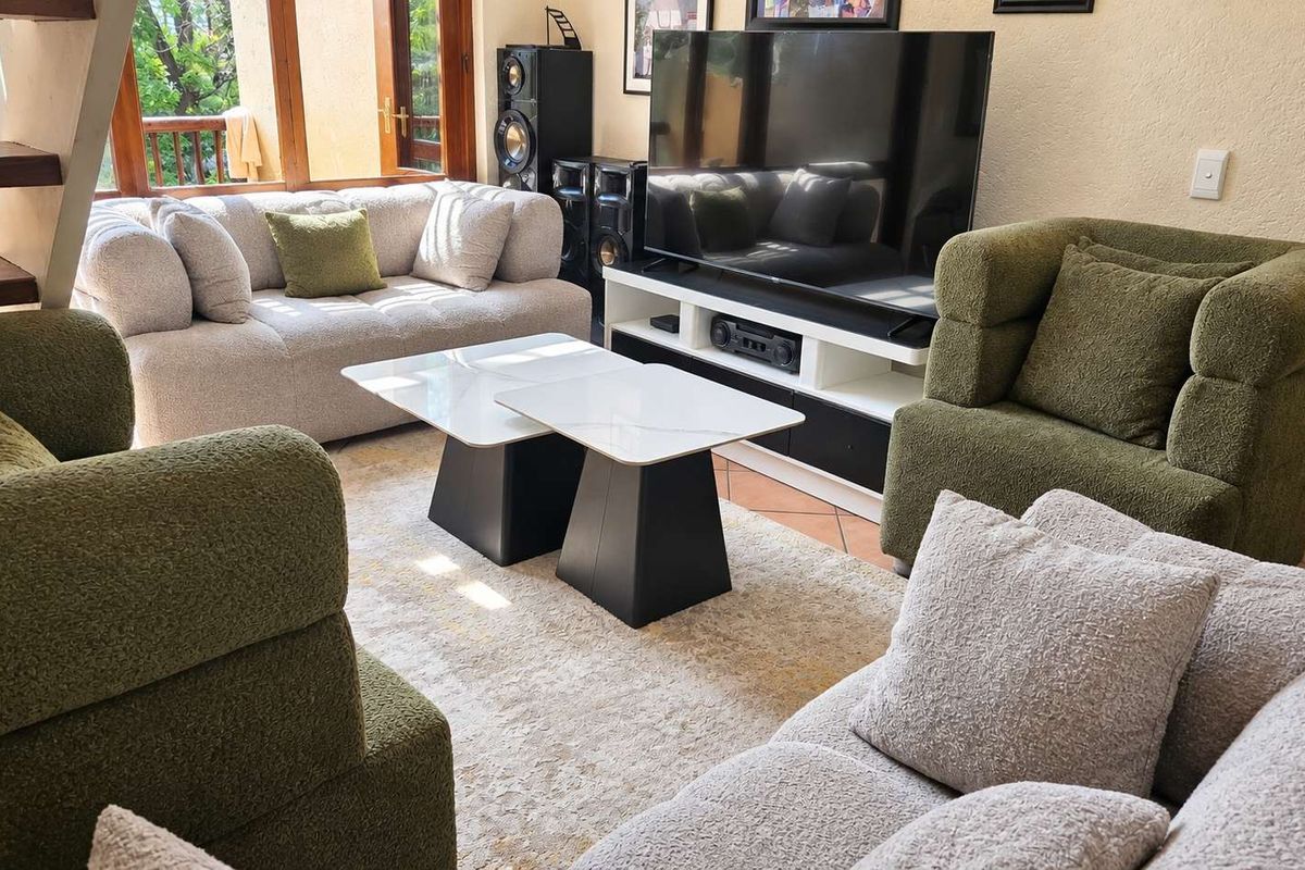 A comfortable living room featuring terracotta floor tiles, wooden window frames, and access to an adjacent outdoor area via a staircase.