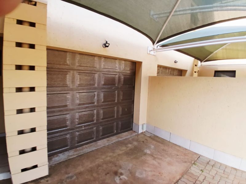 A covered garage area featuring a sectional door, paved driveway, and overhead shade sail structure.