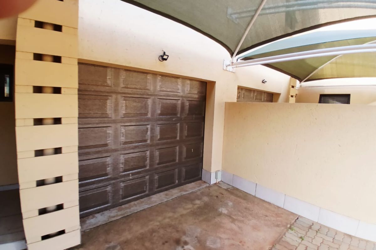 A covered garage area featuring a sectional door, paved driveway, and overhead shade sail structure.