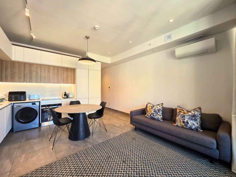 Modern open-plan living area featuring a sleek kitchen with integrated appliances, tiled flooring, and a wall-mounted air conditioning unit.