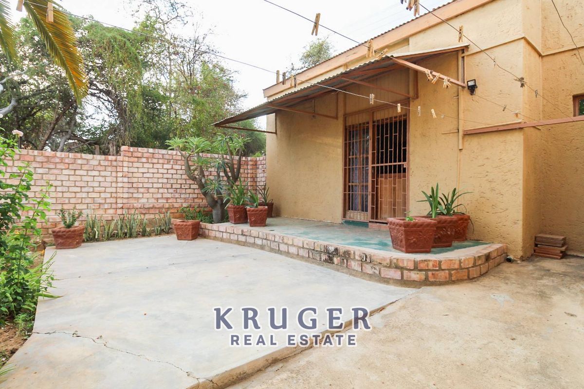 Rear exterior view featuring a concrete patio area, brick boundary wall, and a covered entrance with security gate.