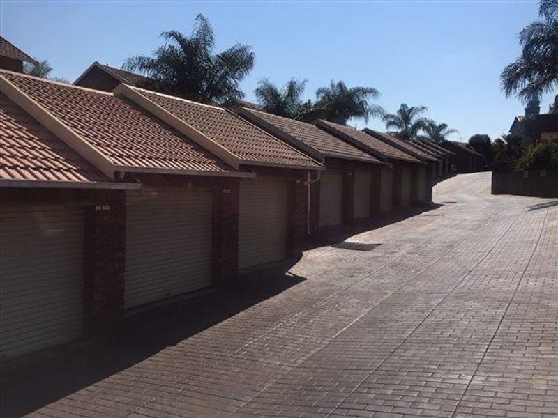A row of residential garages with tiled roofs and roller doors, situated along a paved driveway in a townhouse complex.