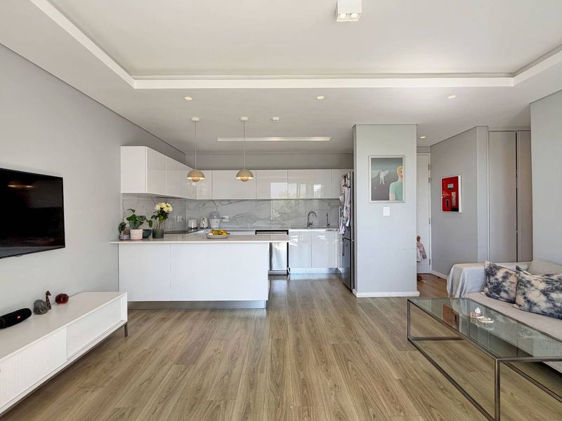 Modern open-plan living area featuring a sleek kitchen with glossy white cabinetry, marble-look backsplash, and a functional island, seamlessly integrated with the living space.