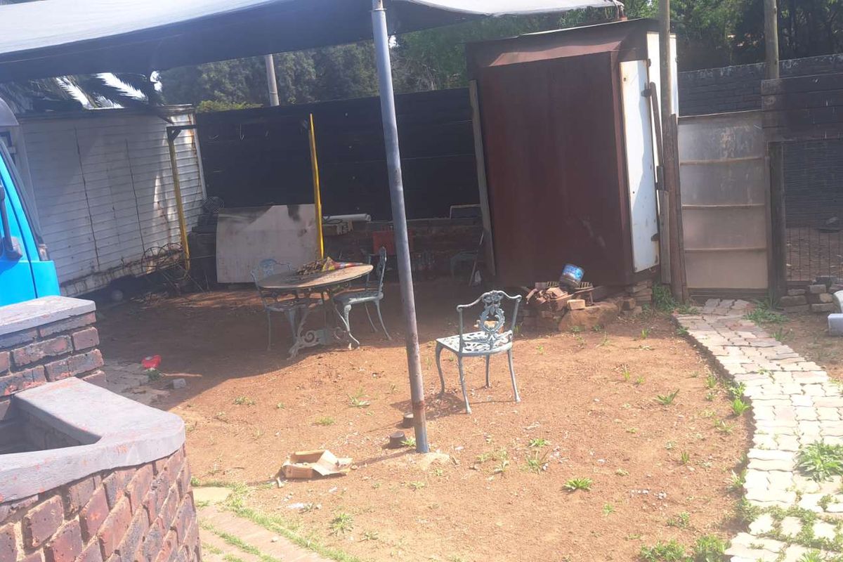 Rear outdoor area featuring a paved pathway, shade sail, and metal storage structure, requiring landscaping and surface improvements.