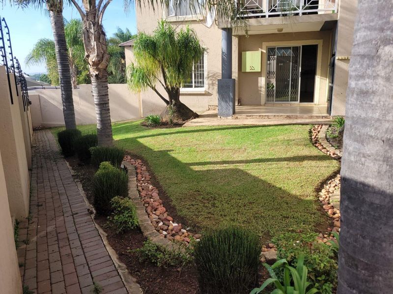 A well-maintained rear garden featuring a paved walkway, landscaped lawn with stone borders, and a covered patio area with sliding door access.