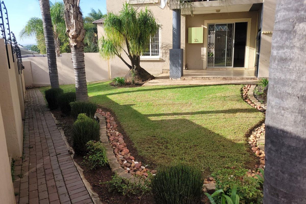 A well-maintained rear garden featuring a paved walkway, landscaped lawn with stone borders, and a covered patio area with sliding door access.