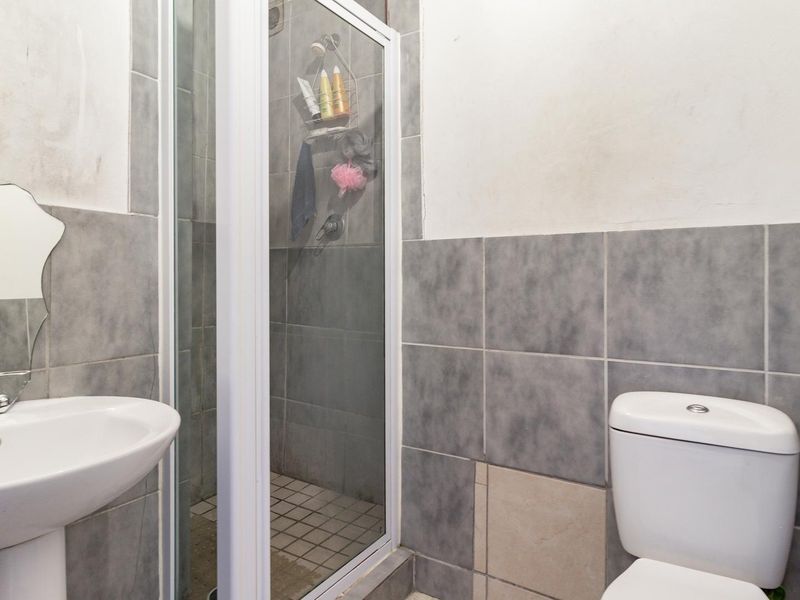 Compact bathroom featuring a pedestal basin, a shower enclosure, and a toilet with partially tiled walls.
