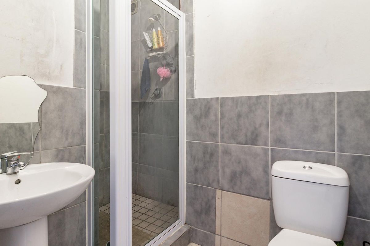 Compact bathroom featuring a pedestal basin, a shower enclosure, and a toilet with partially tiled walls.