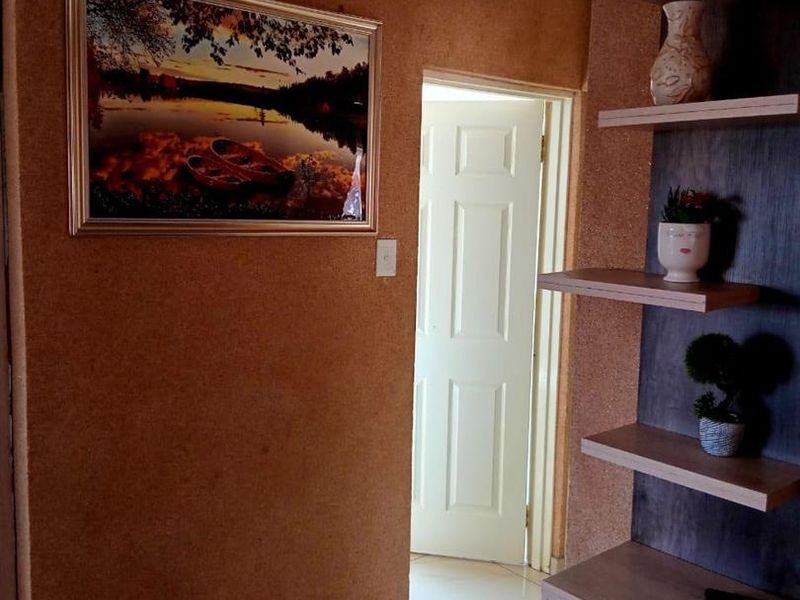 A hallway featuring tiled flooring, textured wall finishes, and a built-in shelving unit leading to an internal doorway.