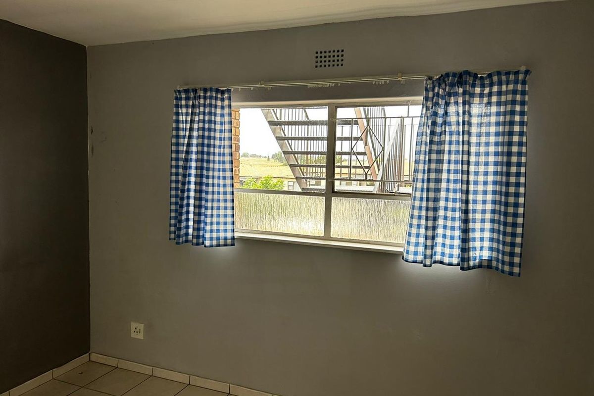 A vacant bedroom featuring tiled flooring, a large window with metal security bars, and neutral grey wall paint.