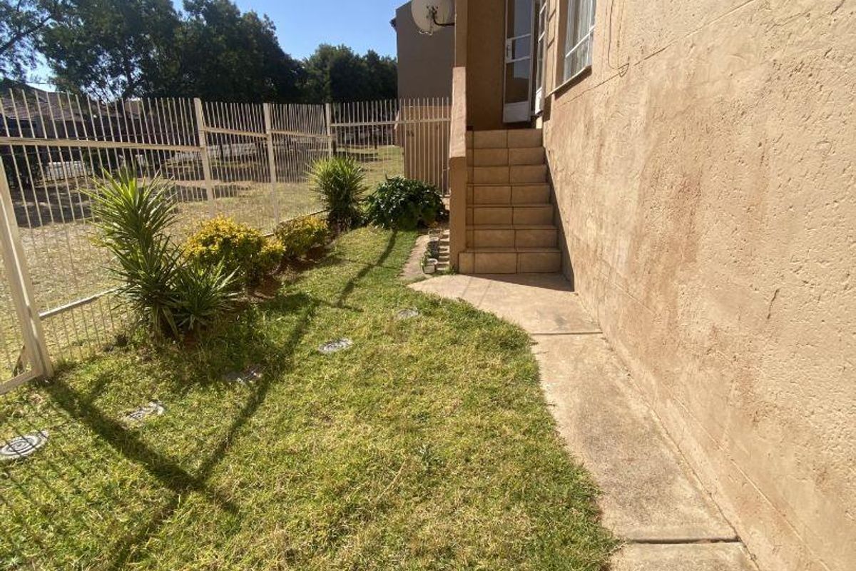 Exterior view of the apartment rear facade featuring a small lawn, concrete pathway, and tiled steps leading to the entrance.