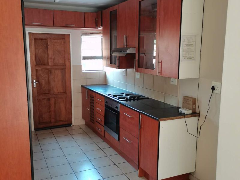 A functional kitchen featuring wood-finish cabinetry, built-in oven with gas hob, tiled flooring, and a rear access door.