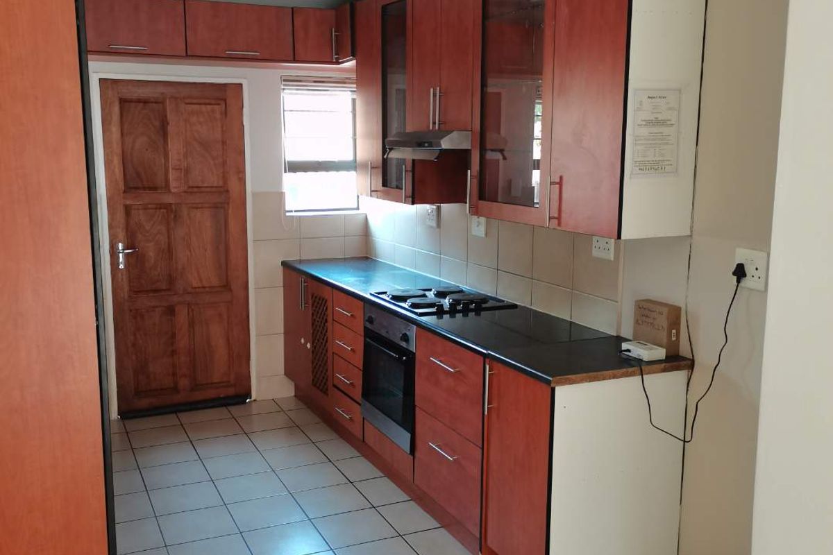 A functional kitchen featuring wood-finish cabinetry, built-in oven with gas hob, tiled flooring, and a rear access door.