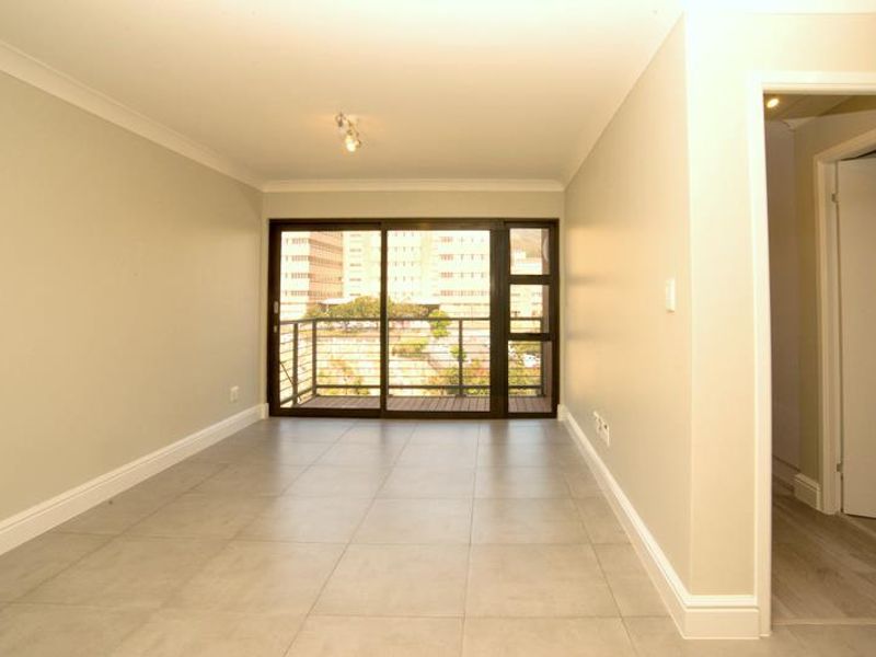 An empty, well-maintained living area featuring neutral tiled flooring, cove cornicing, and a large sliding glass door providing access to a balcony.