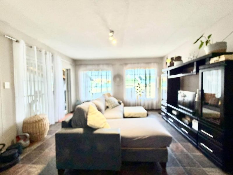 A living room featuring tiled flooring and ceiling-mounted lighting, offering a functional space with natural light from multiple windows.