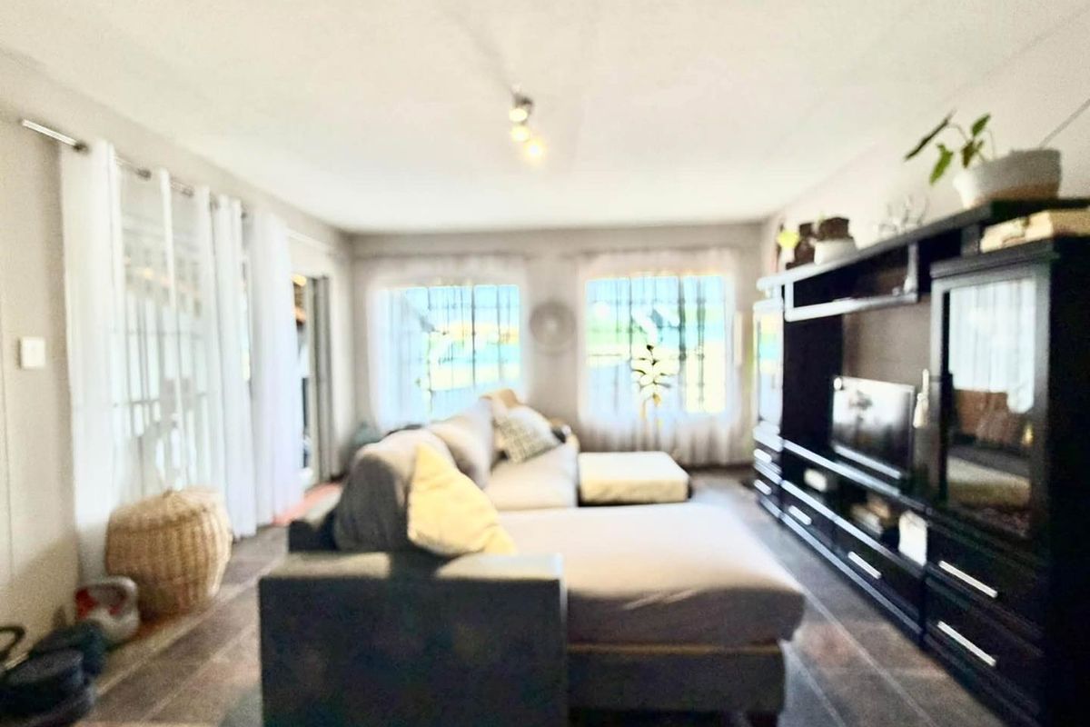 A living room featuring tiled flooring and ceiling-mounted lighting, offering a functional space with natural light from multiple windows.